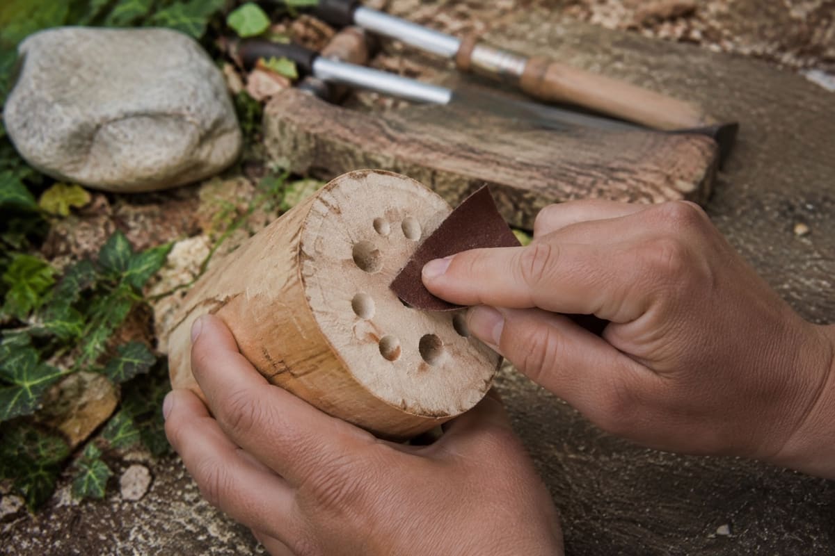 Ein Bohrloch im Holzblock wird mit Schleifpapier entgratet.