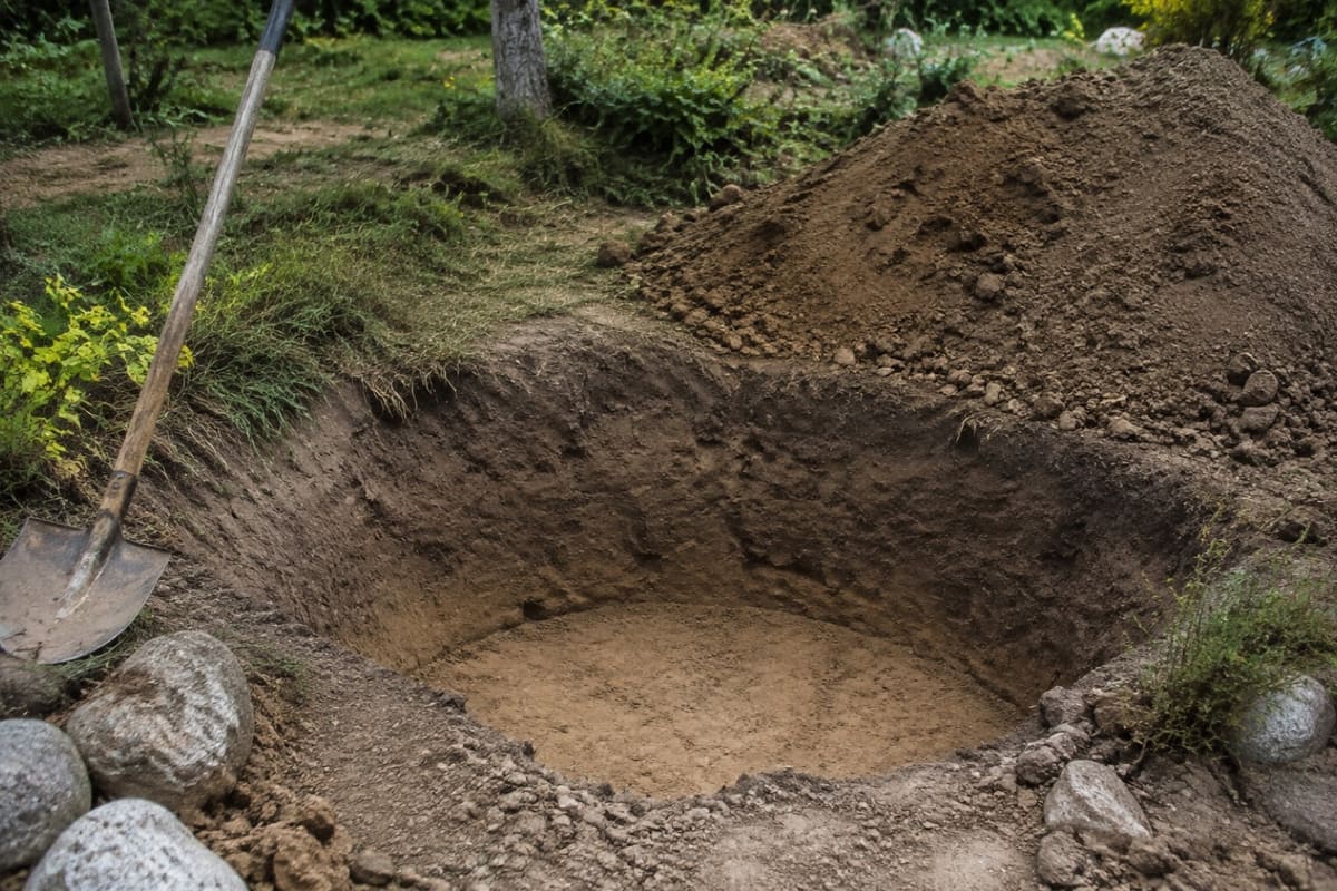 Ausgehobene tiefe Grube für ein Sandarium mit Erdaushub daneben.