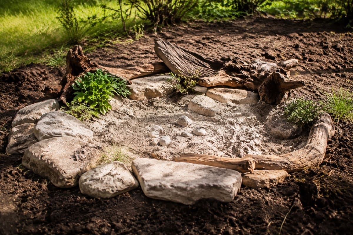 Fertiges Sandarium mit Natursteinen und Totholz am sonnigen Gartenrand.