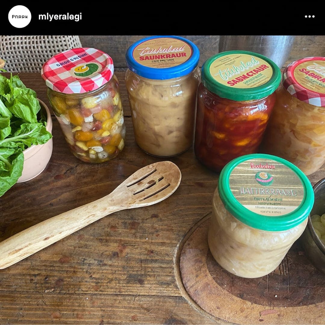 Gläser mit selbst gemachtem Sauerkraut und fermentiertem Gemüse neben frischem Kohl und Krauthobel.